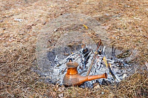 At the stake in the spring forest, a clay Turkish coffee pot is heated against the grass.