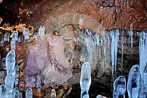 Stalagmite-like ice formations in a lava cave with textured rock walls, showcasing natural winter phenomena.