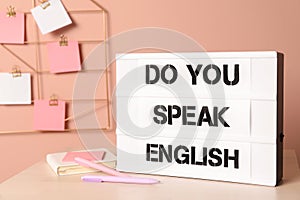Stand with question Do You Speak English and stationery on table near pink wall