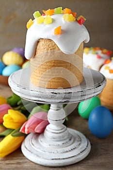 Stand with traditional Easter cake, tulips and colorful eggs on wooden table