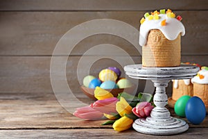 Stand with traditional Easter cake, tulips and colorful eggs on wooden table. Space for text