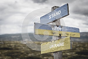 stand with ukraine text quote on wooden signpost outdoors, written on the ukranian flag. Peace and unity concepts