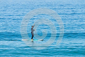 Stand up paddle boarder in wetsuit paddling on a sea. Minimalist image