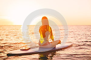 Stand up paddle boarding on a quiet sea with sunset colors. Woman meditation on sup board
