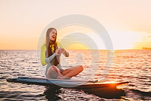 Stand up paddle boarding on a quiet sea with warm summer sunset colors. Happy smiling girl on board at sunset