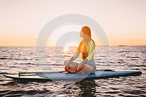 Stand up paddle boarding on a quiet sea with warm sunset colors. Young slim girl is relaxing on ocean