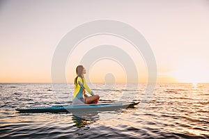 Stand up paddle boarding on a quiet sea with warm sunset colors. Young woman is relaxing on ocean