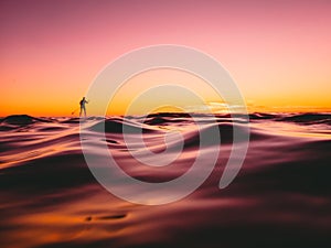 Stand up paddle surfing in ocean with beautiful sunset or sunrise colors