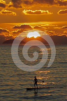 A stand up paddler over the sunset in Camboimhas Beach in Niteroi, Rio de Janeiro