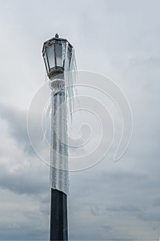 Standalone tall street lamp covered with icicles after a winter freezing storm with grey clouds as background