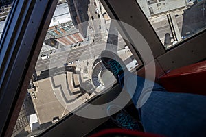 Standing above the abyss - a person in jeans and sneakers stands above a window in the floor from which a panorama of the city