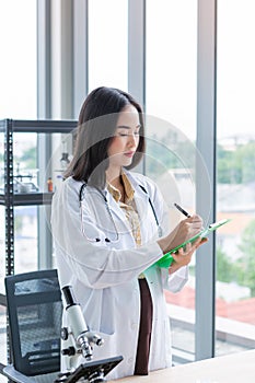 Standing asian nutritionist doctor woman writing on paper green board in laboratory room