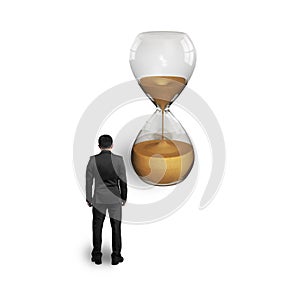 Standing businessman thinking and looking at hourglass