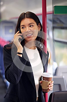 Standing Businesswoman With Takeaway Coffee Commuting To Work On Train Talking On Mobile Phone