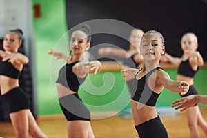 Standing and doing synchronised moves. Group of female kids practicing athletic exercises together indoors