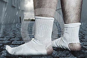 Standing feet with white socks and a big hole standing on cobblestone street. Concept homelessness and poorness