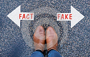 Standing in front of two arrows which show opposite directions, one with the word fact and fake