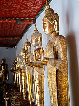 Standing golden Buddha statues in a long line along a wall at the Wat Pho Temple in Bangkok, Thailand