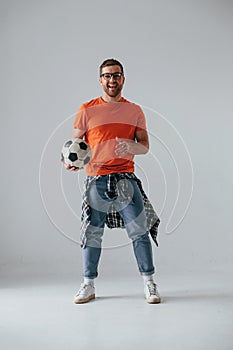 Standing and holding soccer ball. Handsome man is in the studio against white background