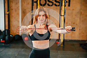 Standing with jump rope. Beautiful strong woman is in the gym