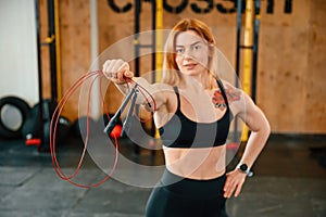 Standing with jump rope. Beautiful strong woman is in the gym