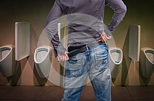 Standing man peeing to a urinal in restroom