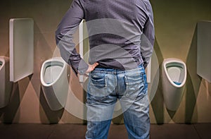 Standing man peeing to a urinal in restroom