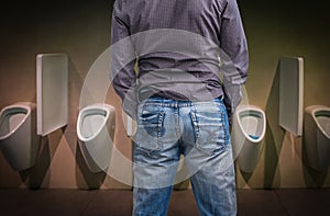 Standing man peeing to a urinal in restroom