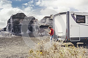 Standing man using mobile phone against a modern camper van and country side rural landscape in background. Concept of travel and