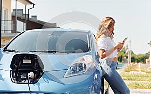 Standing near the car. Young woman in casual clothes with her electromobile outdoors at daytime