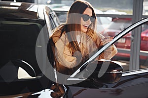Standing near opened window. Fashionable beautiful young woman and her modern automobile