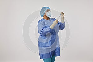 Standing nurse in a coverall PPE uniform against coronavirus holding the COVID-19 vaccine and a syringe