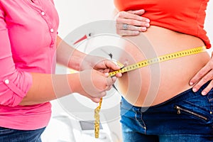 Standing pregnant women and midwife measuring circumference of b
