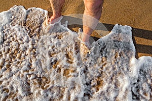 Standing on the shoreline while foaming sea water is surging towards brown sand at sunset. Black Sea