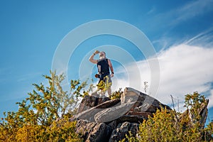 Standing sporty man with backpack on the mountain peak and beautiful mountains atbright sunny day.