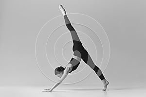 Standing on twine. Black and white photography. Young slim girl doing stretching exercises over studio background