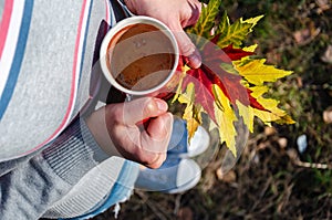 Standing woman holding mug of coffee and colorful autumn leaves. Autumn mood. View from above. Close-up