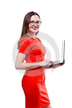 Standing young adult woman in red dress & glasses holding laptop computer - isolated over white background.