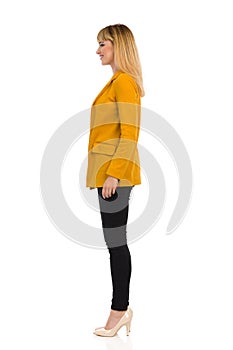 Standing Young Woman In Yellow Jacket And High Heels. Side View
