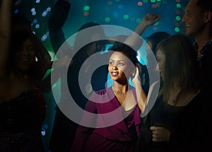 She stands out on the dance floor. Shot of a smiling young woman standing on a dance floor in a nightclub surrounded by