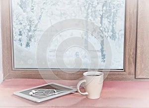 stands on the windowsill of a winter coffee window with a tablet and headphones, with a filter