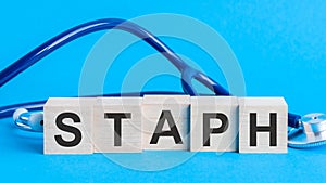 Staph word written on wooden blocks and stethoscope on light blue background