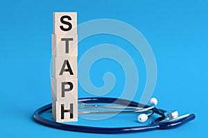 Staph word written on wooden blocks and stethoscope on light blue background