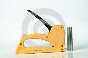 yellow gun tacker with staples, on white background and reflection