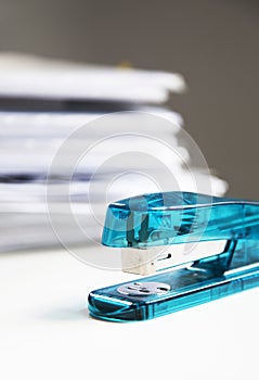 Stapler on white table with stack of papers in background