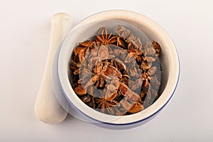 Star anise in a blue ceramic spice mortar with a pestle on a white background. Close up