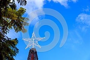 A star atop a Christmas tree, against the blue sky outdoors