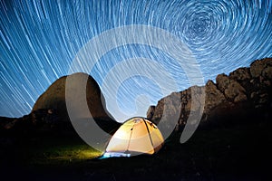 Star circles above the mountains and a glowing camping tent