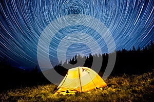 Star circles above the night mountain forest and a glowing camping tent