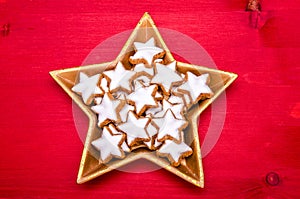 Star shaped christmas cookies in a star shaped golden bowl on a red wooden background